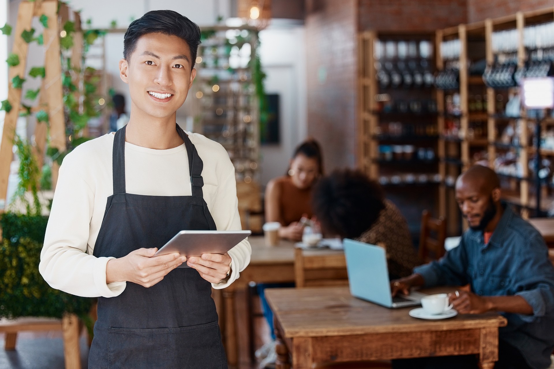 Portrait of smiling asian small business owner in his restaurant holding a wireless digital tablet. Young businessman using a digital tablet to do stocktake and order products online through shopping